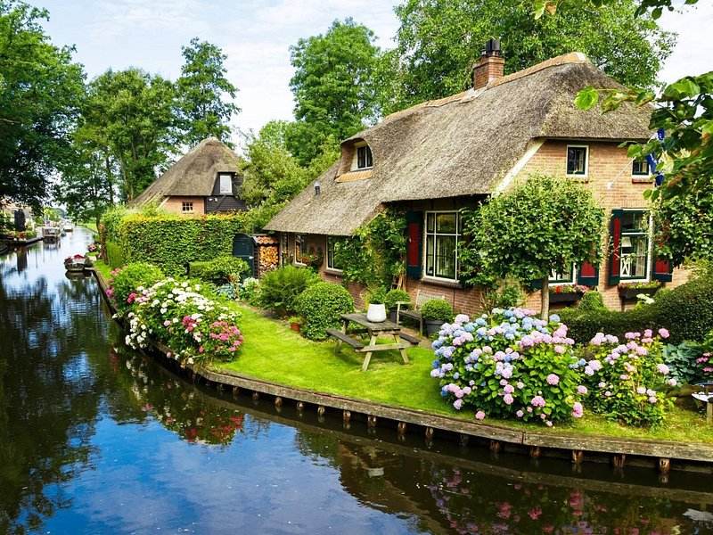 A Giethoorn canal running between thatched cottages and wooden footbridges