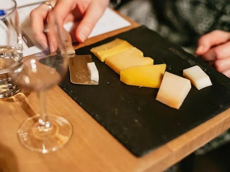Wedges of Dutch farmhouse cheese cut on a board for tasting, beside a glass of wine