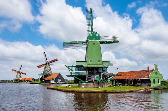 A row of Zaanse Schans windmills and red-roofed barns along the bank of the River Zaan